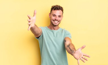 Genç, yakışıklı İspanyol adam neşeyle gülümsüyor sıcak, dostça, sevgi dolu bir kucaklama yapıyor, mutlu ve sevimli hissediyor.