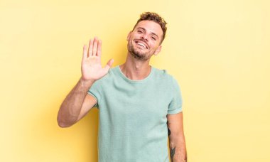 Genç, yakışıklı İspanyol adam mutlu ve neşeyle gülümsüyor, el sallıyor, seni selamlıyor, ya da hoşça kal diyor.