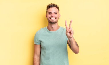 Genç, yakışıklı İspanyol adam gülümsüyor ve arkadaş canlısı görünüyor. İki ya da iki numarayı gösteriyor. Elleri önde, geriye doğru sayıyor.