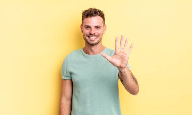 Genç, yakışıklı İspanyol adam gülümsüyor ve arkadaş canlısı görünüyor. 5 ya da 5 numarayı gösteriyor. Eli önde, geriye doğru sayıyor.