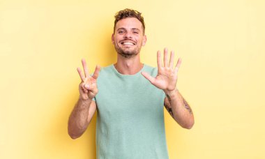 Genç, yakışıklı İspanyol adam gülümsüyor ve arkadaş canlısı görünüyor, 8 ya da 8 numarayı gösteriyor, elleri önde, geriye doğru sayıyor.