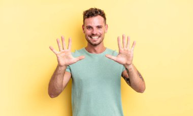 Genç, yakışıklı İspanyol adam gülümsüyor ve arkadaş canlısı görünüyor. Elleri önde ve geriye doğru sayıyor.