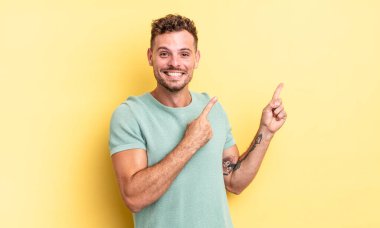 Genç, yakışıklı İspanyol adam mutlu bir şekilde gülümsüyor ve her iki elini de fotokopi alanında objeler gösteriyor.