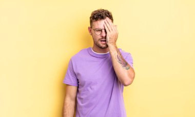 Genç, yakışıklı İspanyol bir adam uykulu, sıkılmış ve esniyor, baş ağrısı ve yüzünün yarısını kaplayan bir elle.