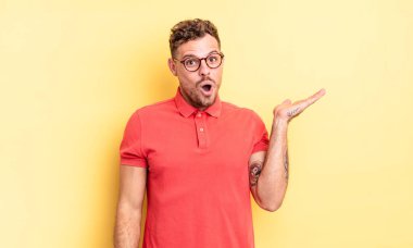 Genç, yakışıklı İspanyol bir adam şaşırmış ve şok olmuş görünüyor, çenesi düşmüş, elinde açık bir elle bir nesne tutuyor.