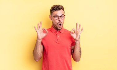 Genç, yakışıklı İspanyol bir adam şok olmuş, şaşırmış ve şaşırmış hissediyor. Onaylıyor. İki eliyle işaret veriyor.