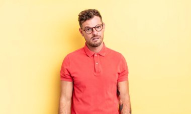 young handsome hispanic man feeling puzzled and confused, with a dumb, stunned expression looking at something unexpected