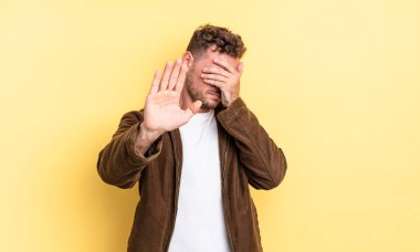 Genç, yakışıklı, İspanyol bir adam elleriyle yüzünü örtüyor ve diğer elini kamerayı durdurmak için öne koyuyor. Fotoğraf ya da resimleri reddediyor.