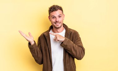 Genç, yakışıklı İspanyol adam neşeyle gülümsüyor ve yan taraftaki fotokopi alanını işaret ederek bir nesneyi gösteriyor ya da reklamını yapıyor.