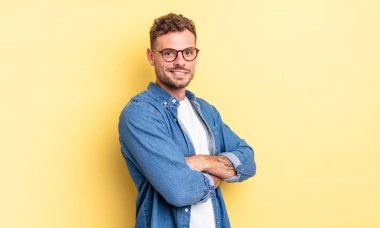 Genç, yakışıklı İspanyol adam kameraya çapraz kollarıyla gülümsüyor ve mutlu, kendinden emin, tatmin olmuş bir yüz ifadesi var.