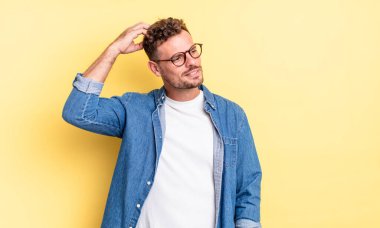 Genç, yakışıklı İspanyol adam şaşkın ve şaşkın hissediyor, başını kaşıyor ve yana bakıyor.