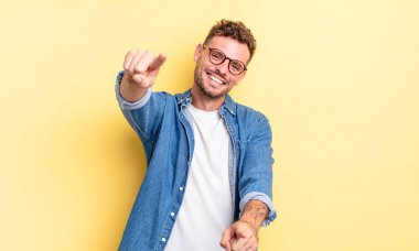 Genç, yakışıklı İspanyol bir adam mutlu ve kendinden emin, kameraya iki eliyle bakıyor ve gülüyor, seni seçiyor.