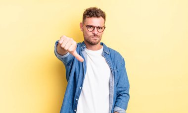 Genç, yakışıklı İspanyol bir adam sinirli, sinirli, hayal kırıklığına uğramış ya da hoşnutsuz, ciddi bir bakışla başparmağını kaldırıyor.