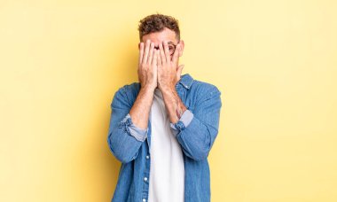 Genç, yakışıklı İspanyol adam elleriyle yüzünü kapatıyor, parmaklarının arasından şaşkın bir ifadeyle yan tarafa bakıyor.