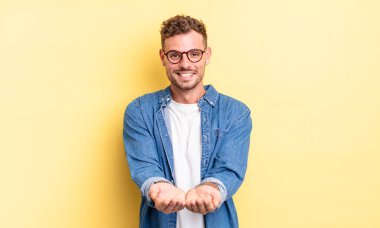 Genç, yakışıklı İspanyol adam mutlu bir şekilde gülümsüyor arkadaş canlısı, kendinden emin, olumlu bakışlı, bir nesne ya da konsept sunuyor ve gösteriyor.