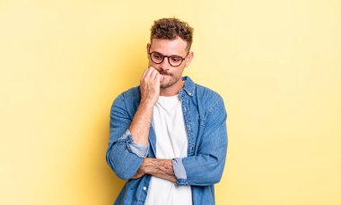 Genç, yakışıklı İspanyol bir adam ciddi, düşünceli ve endişeli hissediyor. Eli çenesine değmiş şekilde yan yan bakıyor.