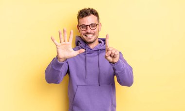 Genç, yakışıklı İspanyol adam gülümsüyor ve arkadaş canlısı görünüyor. Altı ya da altıncı numarayı gösteriyor. Elleri önde, geri sayıyor.