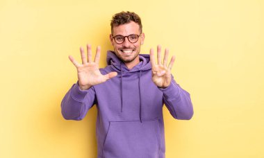 Genç, yakışıklı İspanyol adam gülümsüyor ve arkadaş canlısı görünüyor. 9 ya da 9 numarayı gösteriyor. Elleri önde ve geri sayıyor.