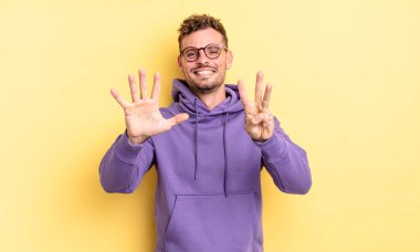 Genç, yakışıklı İspanyol adam gülümsüyor ve arkadaş canlısı görünüyor, 8 ya da 8 numarayı gösteriyor, elleri önde, geriye doğru sayıyor.