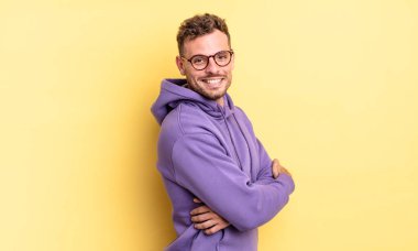 Genç, yakışıklı İspanyol adam neşeyle gülümsüyor, mutlu, tatmin olmuş ve rahatlamış hissediyor, kollarını kavuşturup yan tarafa bakıyor.