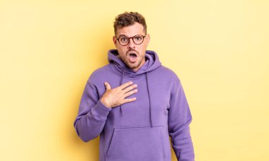 Genç, yakışıklı İspanyol adam şok olmuş, şaşırmış ve şaşırmış hissediyor, elleri göğsünde ve ağzı açık, kim olduğumu söylüyor, ben?