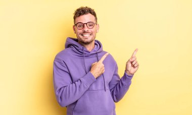 Genç, yakışıklı İspanyol adam mutlu bir şekilde gülümsüyor ve her iki elini de fotokopi alanında objeler gösteriyor.