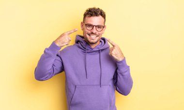 Genç, yakışıklı İspanyol adam, kendine güvenerek gülümsüyor. Geniş gülümseme, pozitif, rahat, tatmin olmuş tavır.