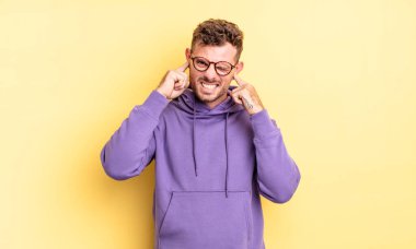 Genç, yakışıklı İspanyol bir adam sinirli, stresli ve sinirli görünüyor, iki kulağını da sağır edici bir ses, ses ya da yüksek sesle kapatıyor.