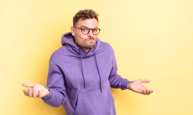 young handsome hispanic man feeling clueless and confused, having no idea, absolutely puzzled with a dumb or foolish look