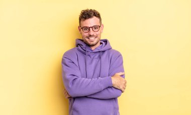 Genç, yakışıklı İspanyol bir adam mutlu, gururlu ve memnun görünüyor. Kollarını kavuşturup gülümsüyor.