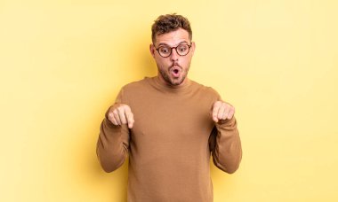 Genç, yakışıklı, ağzı açık, iki eliyle aşağıya doğru bakan, şaşkın, şaşkın ve şaşırmış görünen İspanyol bir adam.