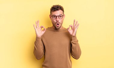 Genç, yakışıklı İspanyol bir adam şok olmuş, şaşırmış ve şaşırmış hissediyor. Onaylıyor. İki eliyle işaret veriyor.