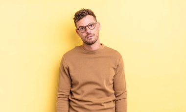 young handsome hispanic man feeling puzzled and confused, with a dumb, stunned expression looking at something unexpected