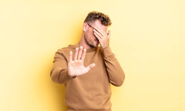 Genç, yakışıklı, İspanyol bir adam elleriyle yüzünü örtüyor ve diğer elini kamerayı durdurmak için öne koyuyor. Fotoğraf ya da resimleri reddediyor.