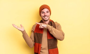 Genç, yakışıklı İspanyol adam neşeyle gülümsüyor ve yan taraftaki fotokopi alanını işaret ederek bir nesneyi gösteriyor ya da reklamını yapıyor.