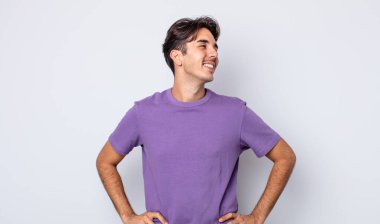 Genç, yakışıklı İspanyol adam mutlu, neşeli ve kendinden emin görünüyor, gururla gülümsüyor ve iki elini de kalçasında istiyor.