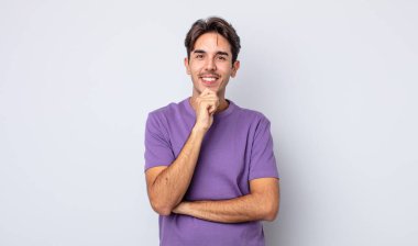 Genç, yakışıklı, İspanyol bir adam mutlu görünüyor ve eli çenesinde gülümsüyor, merak ediyor ya da soru soruyor, seçenekleri karşılaştırıyor.