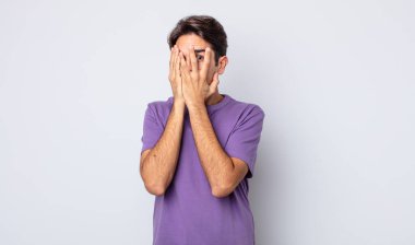 Genç, yakışıklı İspanyol adam elleriyle yüzünü kapatıyor, parmaklarının arasından şaşkın bir ifadeyle yan tarafa bakıyor.