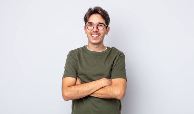 Genç, yakışıklı İspanyol bir adam mutlu, gururlu ve memnun görünüyor. Kollarını kavuşturup gülümsüyor.