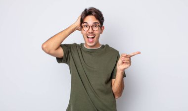 Genç, yakışıklı İspanyol adam gülüyor, mutlu, pozitif ve şaşırmış görünüyor, yanal fotokopi alanını işaret eden harika bir fikri fark ediyor.