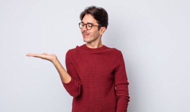 Genç, yakışıklı, İspanyol bir adam mutlu ve gülümsüyor. Yanında duran bir nesneye ya da konsepte bakıyor.