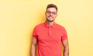 Genç, yakışıklı İspanyol adam neşeli ve rahat bir ifadeyle mutlu, kendinden emin ve rahat bir şekilde gülümsüyor.