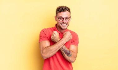 Genç, yakışıklı İspanyol adam sevinçle gülümsüyor ve kutluyor, yumruklarını sıkıp kollarını kavuşturuyor, mutlu ve pozitif hissediyor.