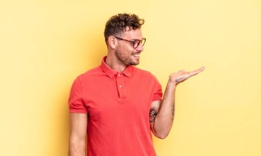 Genç, yakışıklı, İspanyol bir adam mutlu ve gülümsüyor. Yanında duran bir nesneye ya da konsepte bakıyor.