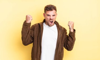 Genç, yakışıklı İspanyol bir adam öfkeli bir ifadeyle agresif bir şekilde bağırıyor ya da yumruklarıyla başarıyı kutluyor.