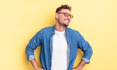 Genç, yakışıklı İspanyol adam mutlu, neşeli ve kendinden emin görünüyor, gururla gülümsüyor ve iki elini de kalçasında istiyor.