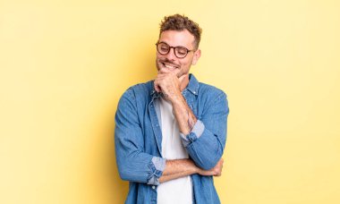 Genç, yakışıklı İspanyol bir adam mutlu, kendinden emin bir ifadeyle gülümsüyor. Elleri çenesinde, merak ediyor ve yan tarafa bakıyor.