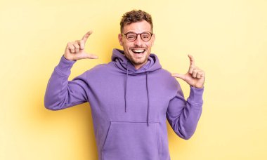 Genç, yakışıklı, İspanyol asıllı bir adam iki eliyle kendi gülümsemesini çiziyor. Olumlu ve mutlu görünüyor. Sağlık kavramı.