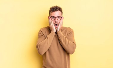 Genç, yakışıklı İspanyol adam şok olmuş ve korkmuş hissediyor, ağzı açık ve elleri yanaklarında korkmuş görünüyor.