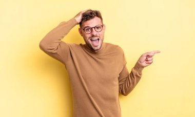 Genç, yakışıklı İspanyol adam gülüyor, mutlu, pozitif ve şaşırmış görünüyor, yanal fotokopi alanını işaret eden harika bir fikri fark ediyor.